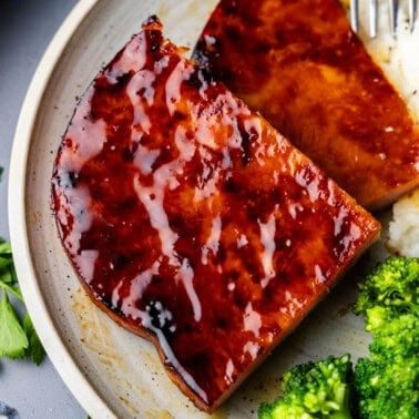 slice of maple and mustard glazed ham steak on plate with broccoli and mashed potatoes