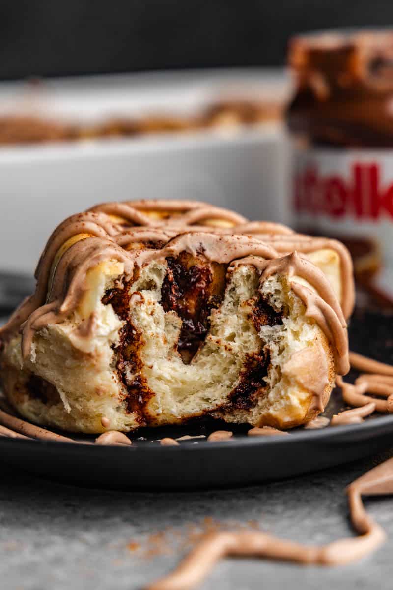 A close up view of a Nutella cinnamon roll that has had a bite taken out revealing the Nutella swirl inside.