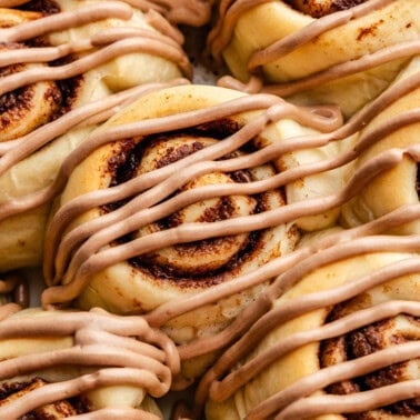 A close up view of nutella cinnamon rolls in a pan, topped with a drizzle of nutella frosting.