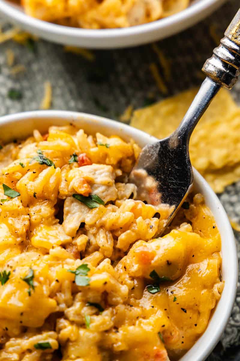 A close-up of a fork scooping out bites of queso chicken and rice.