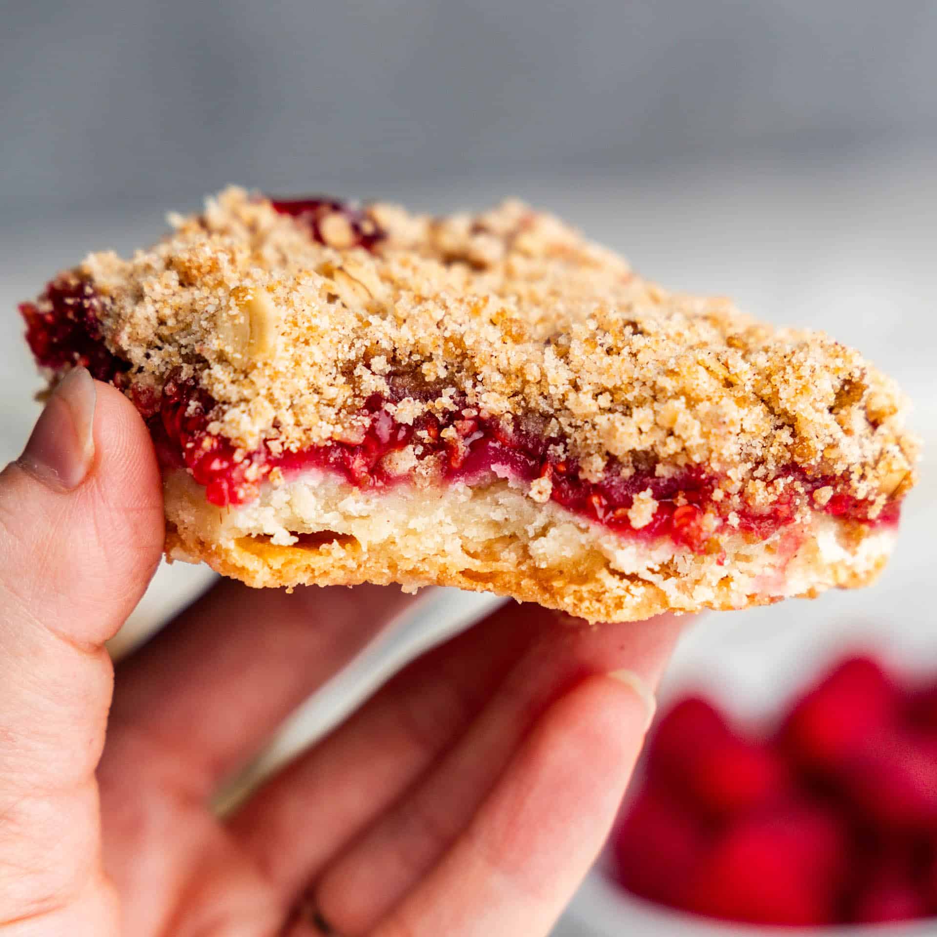 hand holding slice of raspberry streusel bar with bite taken out of it