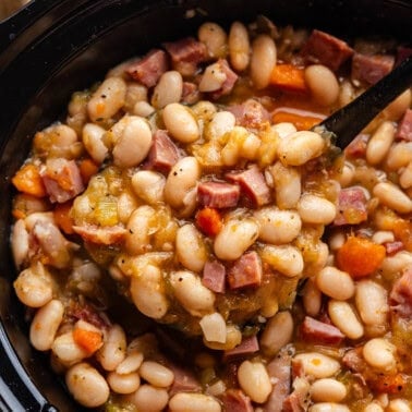 An overhead view of a slow cooker of ham and beans with a ladle dishing out a scoop.