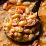 A closeup view of a ladle scooping out a helping of slow cooker ham and beans from the crockpot.