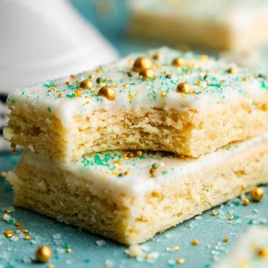 Two sugar cookie bars stacked on top of each other. The top one has a bite taken out of it.