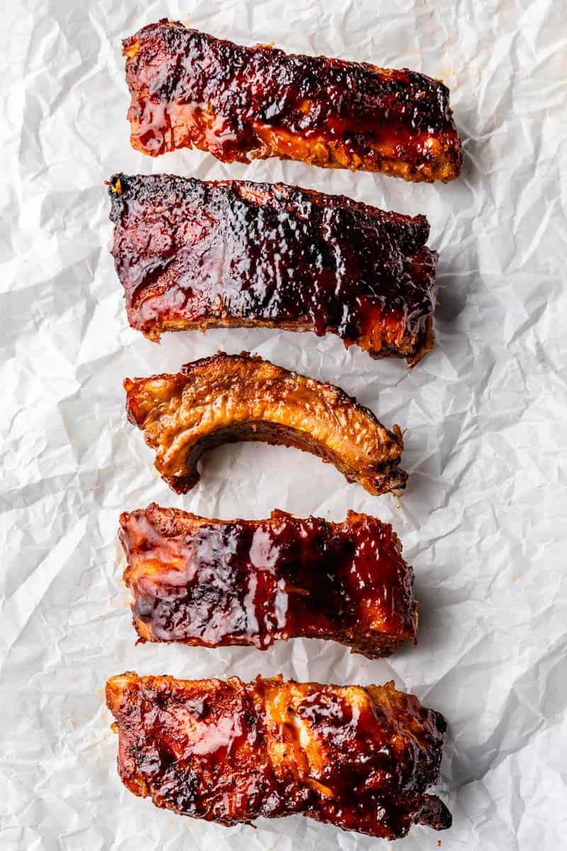 Individual saucy pork ribs lined up on parchment paper.