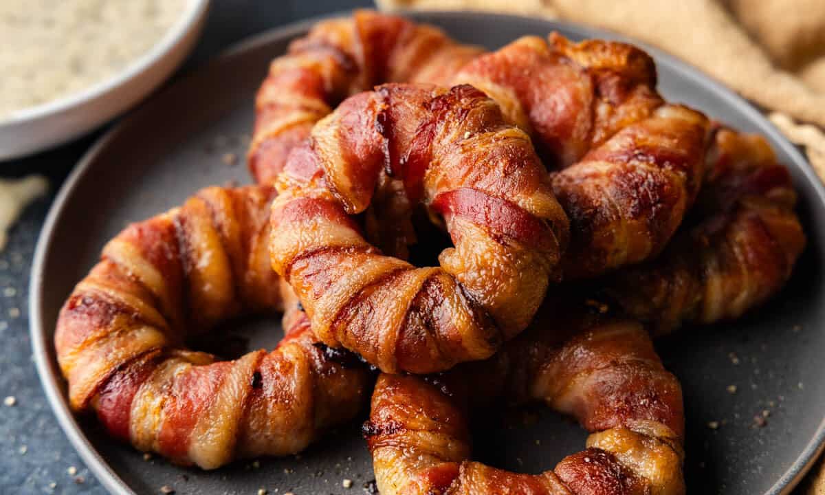 A plate of piled bacon wrapped sausage filled onion rings.