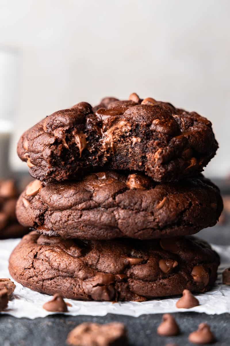 A stack of 3 chocolate chunk cookies on a golden plate with a bite taken out.