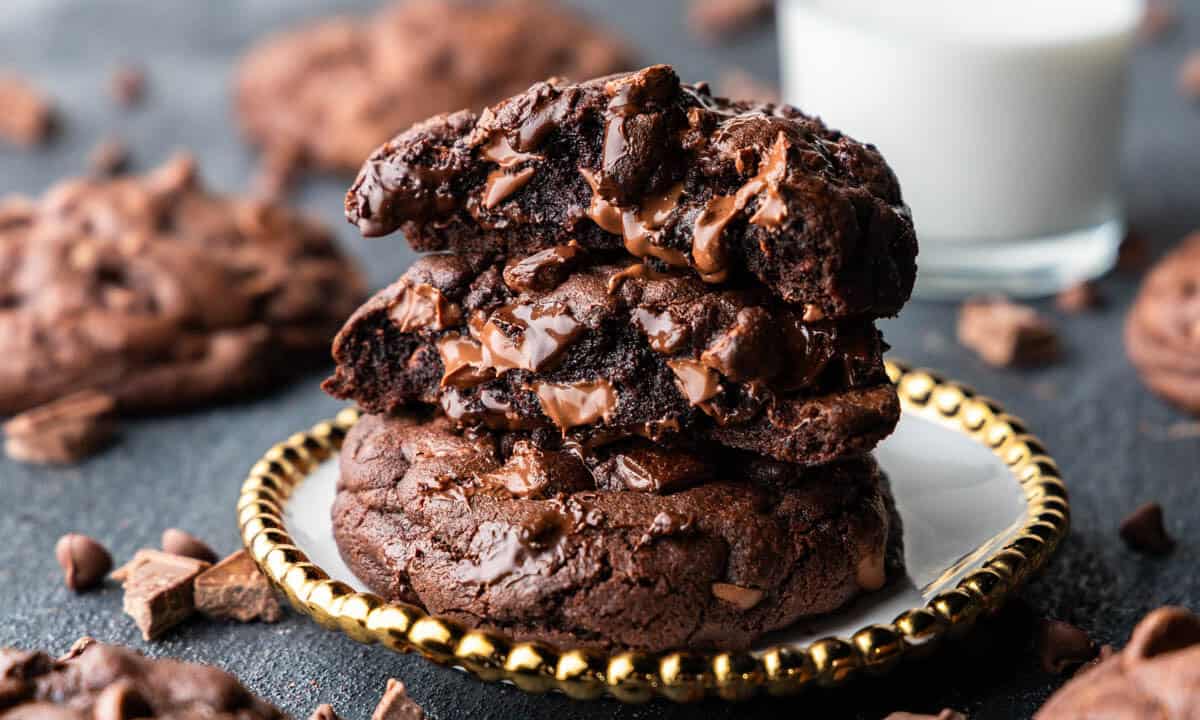 A horizontal image of a stack of 3 ooey gooey chocolate chunk cookies on a golden plate.