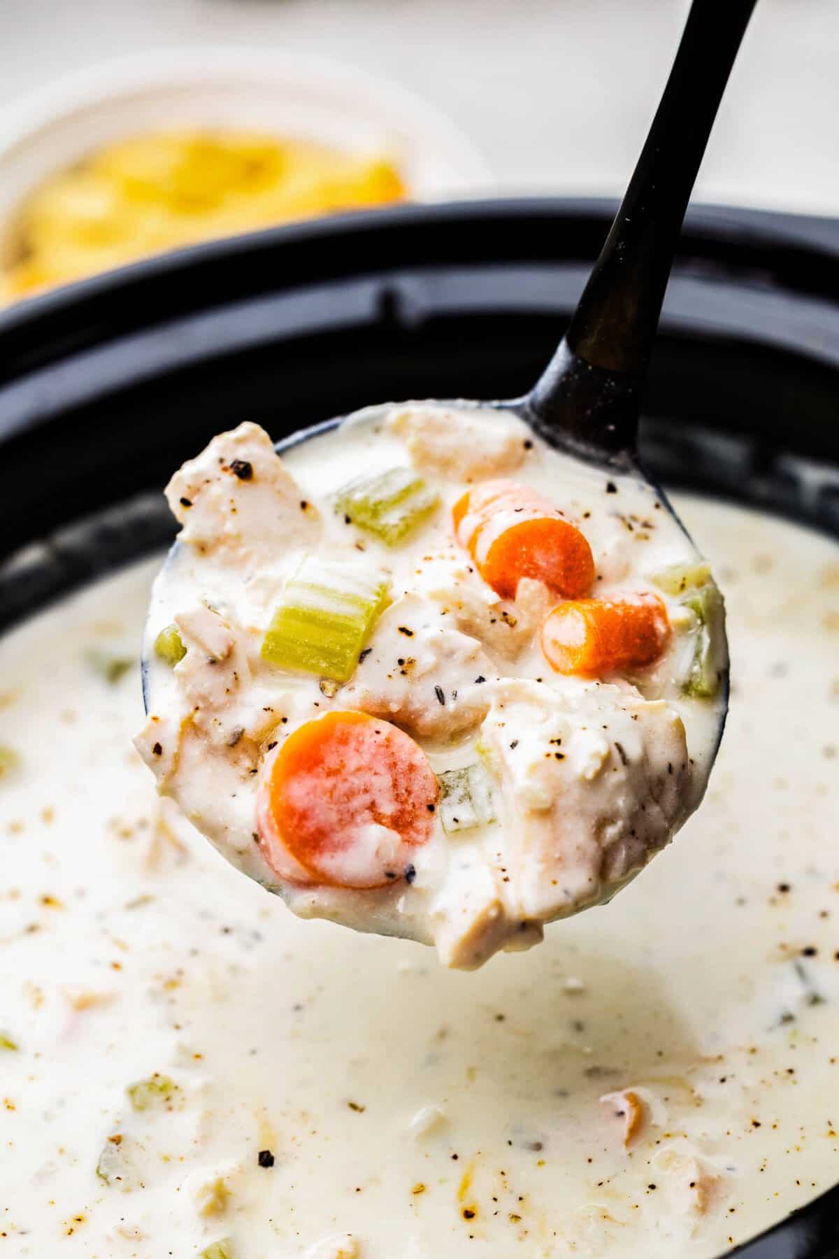 A ladle of creamy chicken soup being lifted out of a slow cooker.