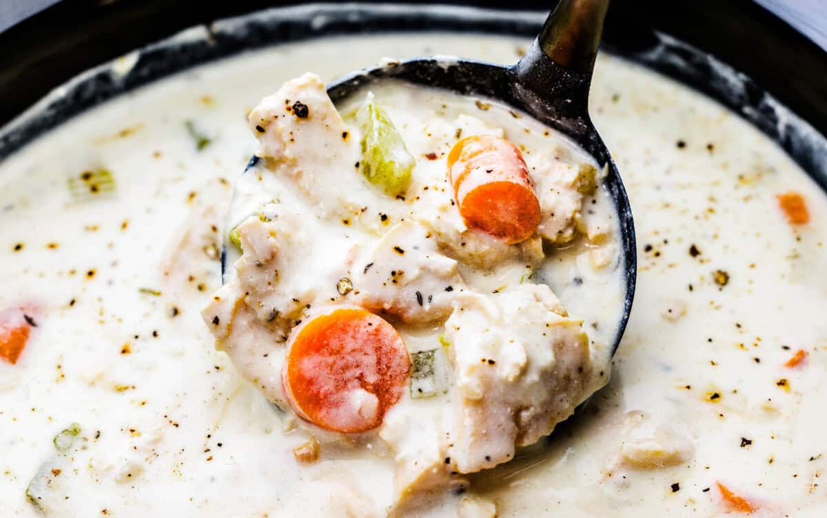 Creamy chicken soup in a ladle in a slow cooker.