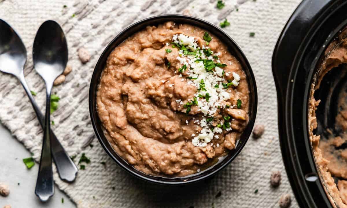 Overhead shot of cooked pinto beans in a bowl next to slow cooker.