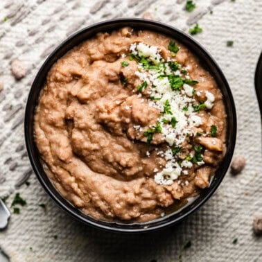 Overhead shot of cooked pinto beans in a bowl next to slow cooker.