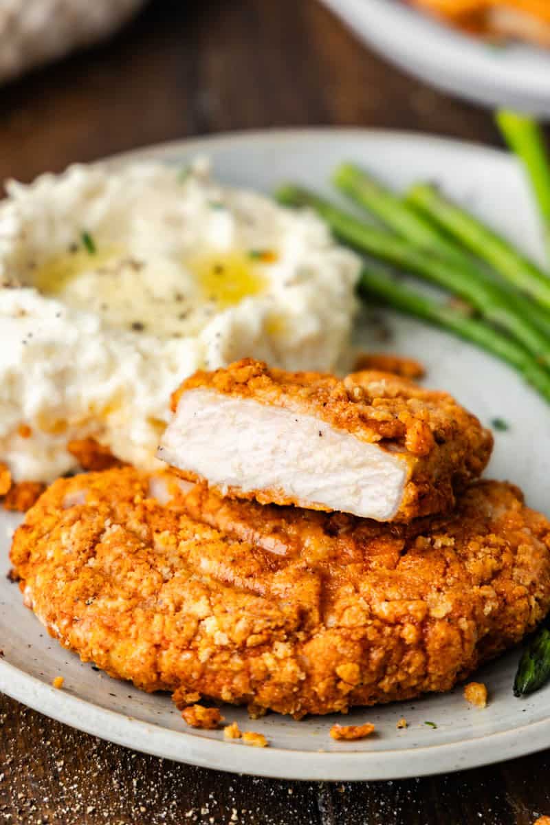 Close up shot of Air fryer crispy pork chops, cut in half on a plate with mashed potatoes and asparagus.