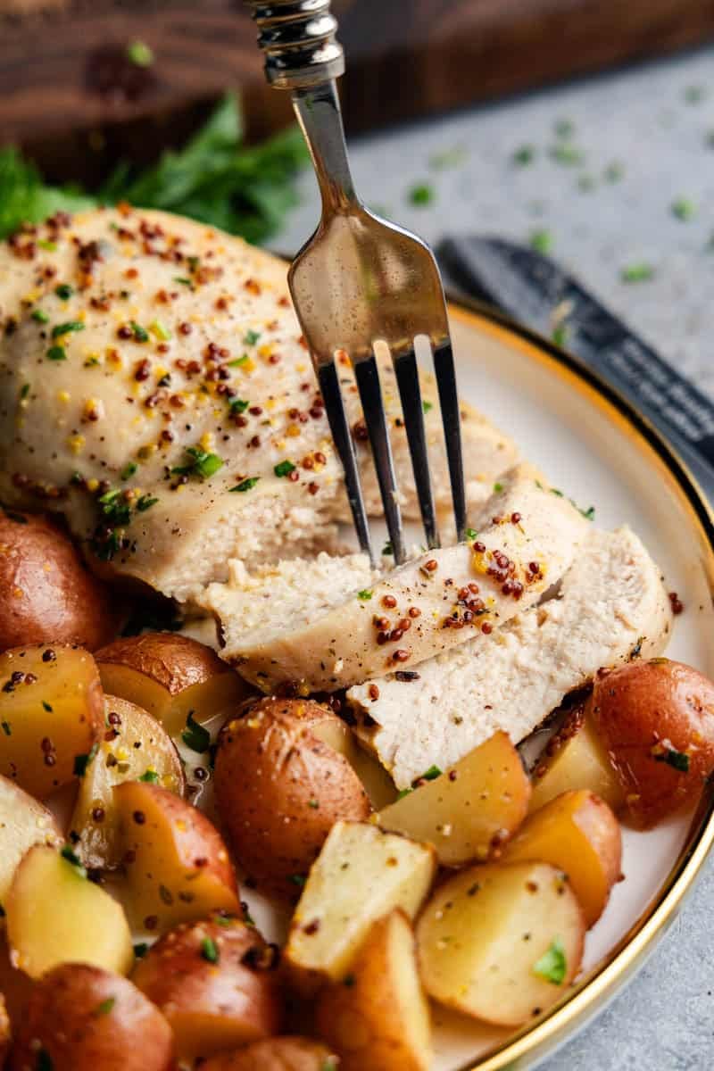 Fork bite of Baked Honey Dijon Chicken and Potatoes on a plate with mini potatoes.