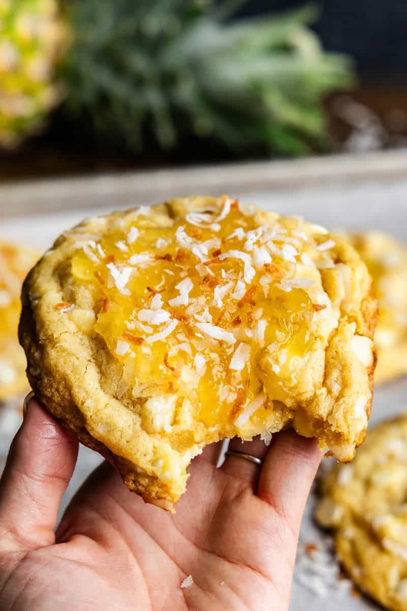 Hand holding a Bakery Style Pina Colada Cookie with a bite taken out of it.