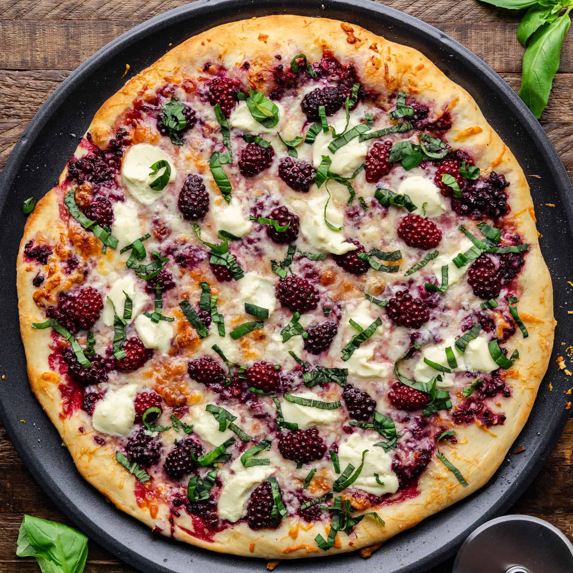 Overhead shot of entire Blackberry Basil Ricotta Pizza on a black plate.