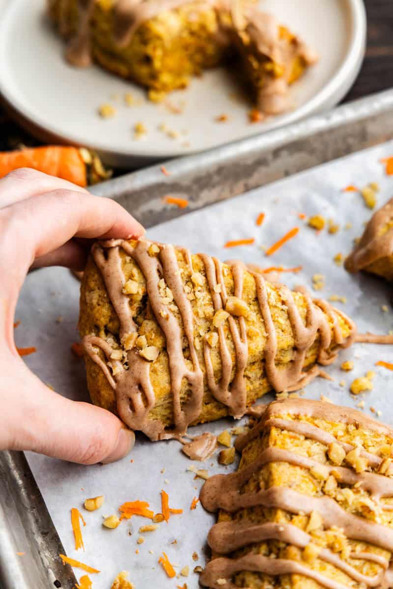 Hand Grabbing a carrot cake scone off a cookie sheet.