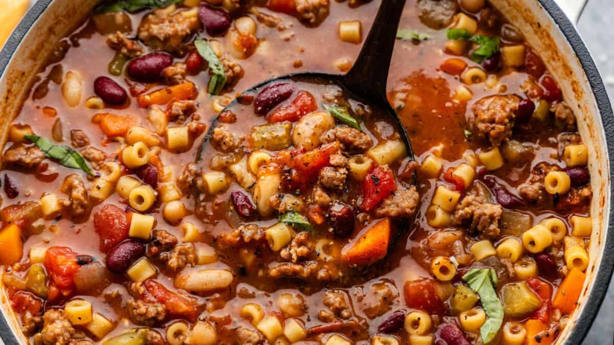 Heaping ladle full of Pasta e Fagioli in a pot.