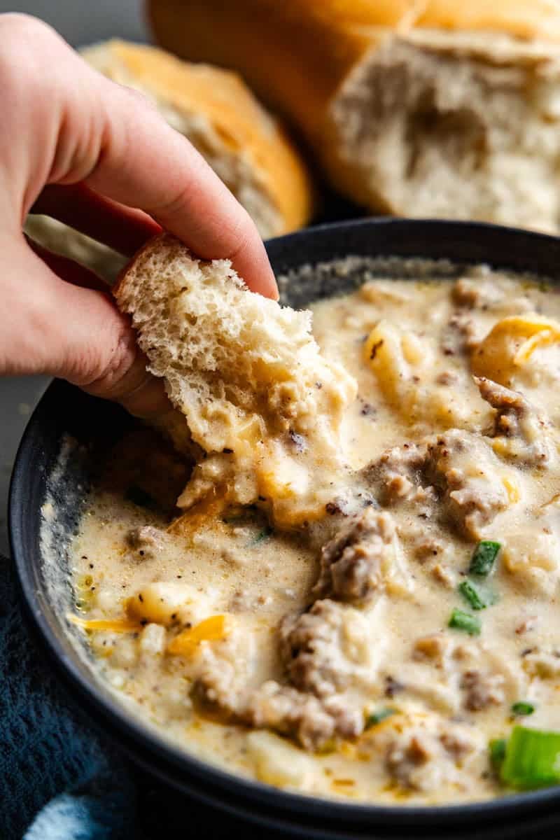 Closeup shot of Creamy Sausage Potato Soup in a bowl with bread being dipped in it.