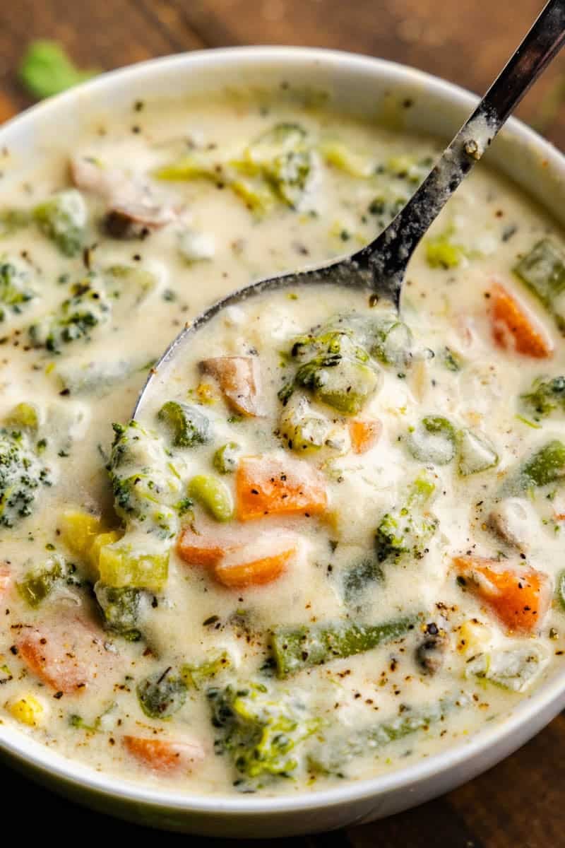 Close up shot of Creamy Vegetable Soup in bowl filling a spoon with soup.