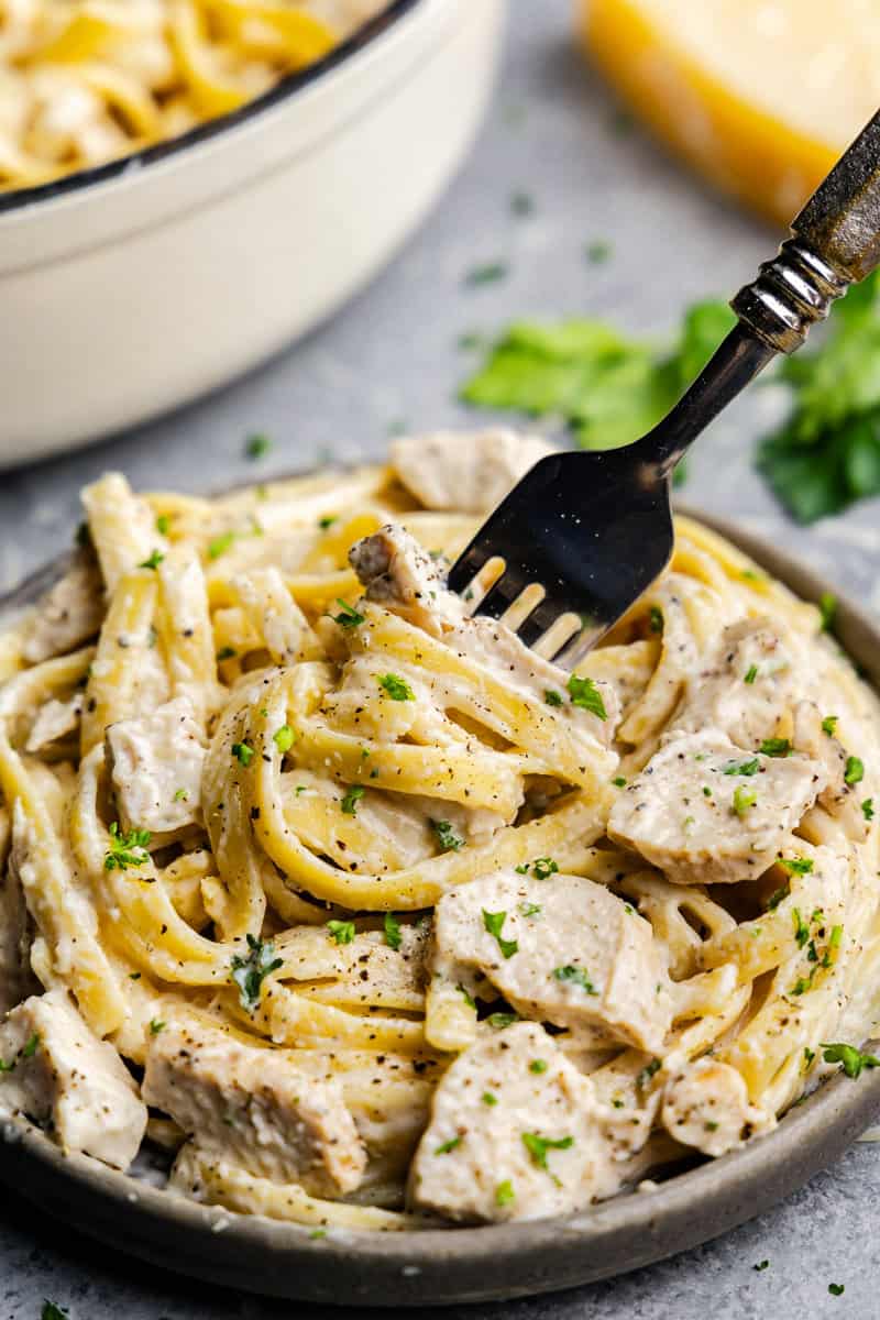 A closeup of a fork twisting pasta and chicken from a plate of chicken alfredo.