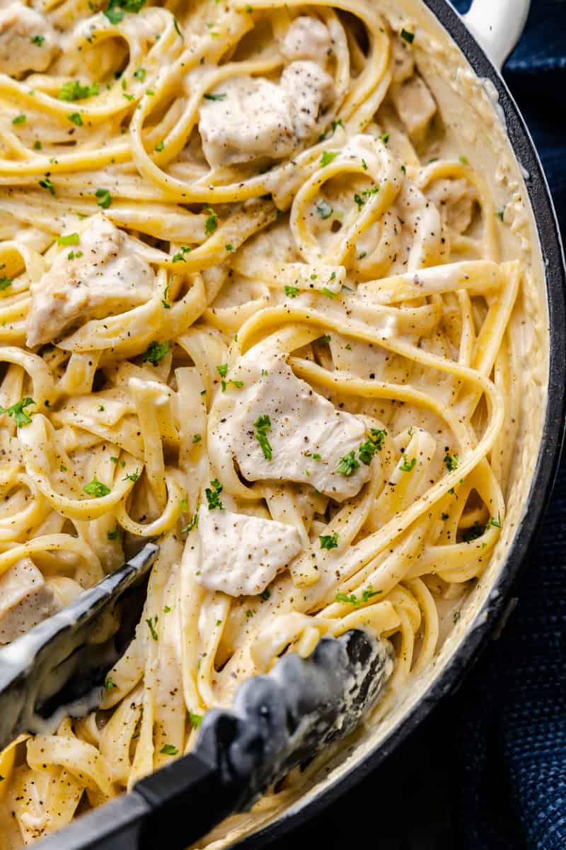 A cast-iron pot of chicken alfredo with parsley and pepper garnish.
