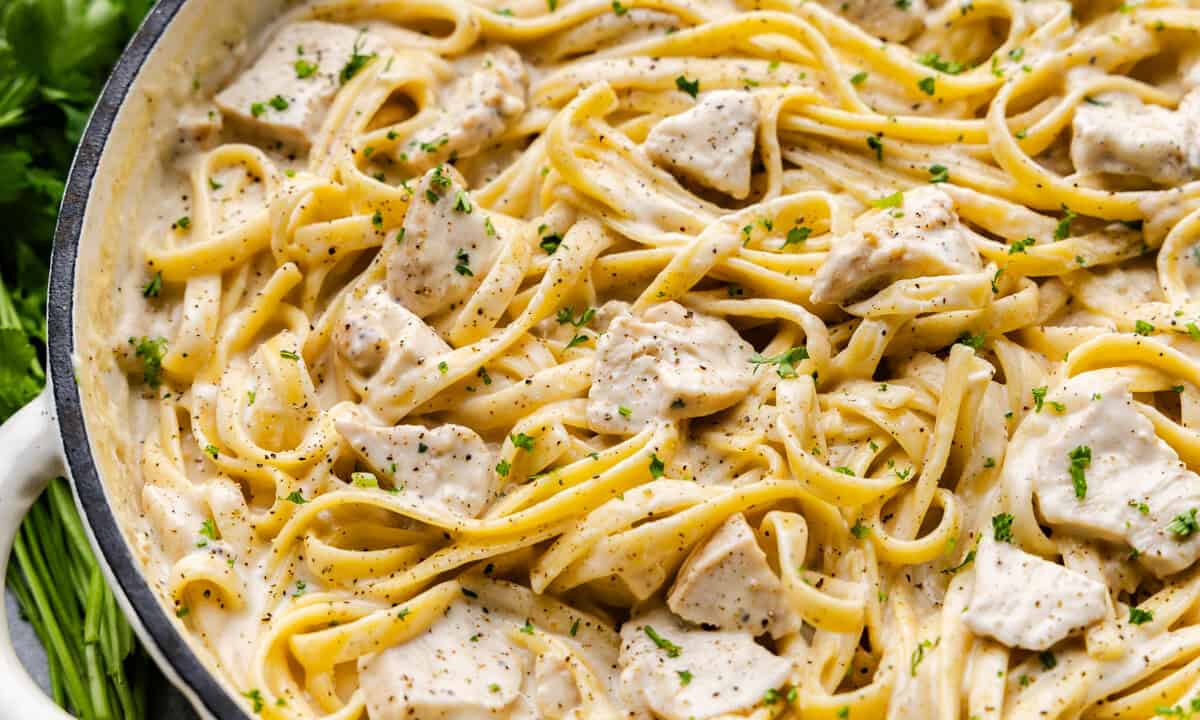A cast-iron pot of chicken alfredo with parsley and pepper garnish.