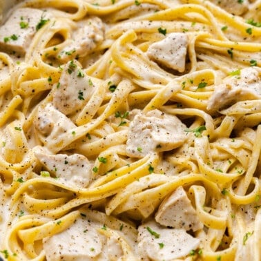 A cast-iron pot of chicken alfredo with parsley and pepper garnish.