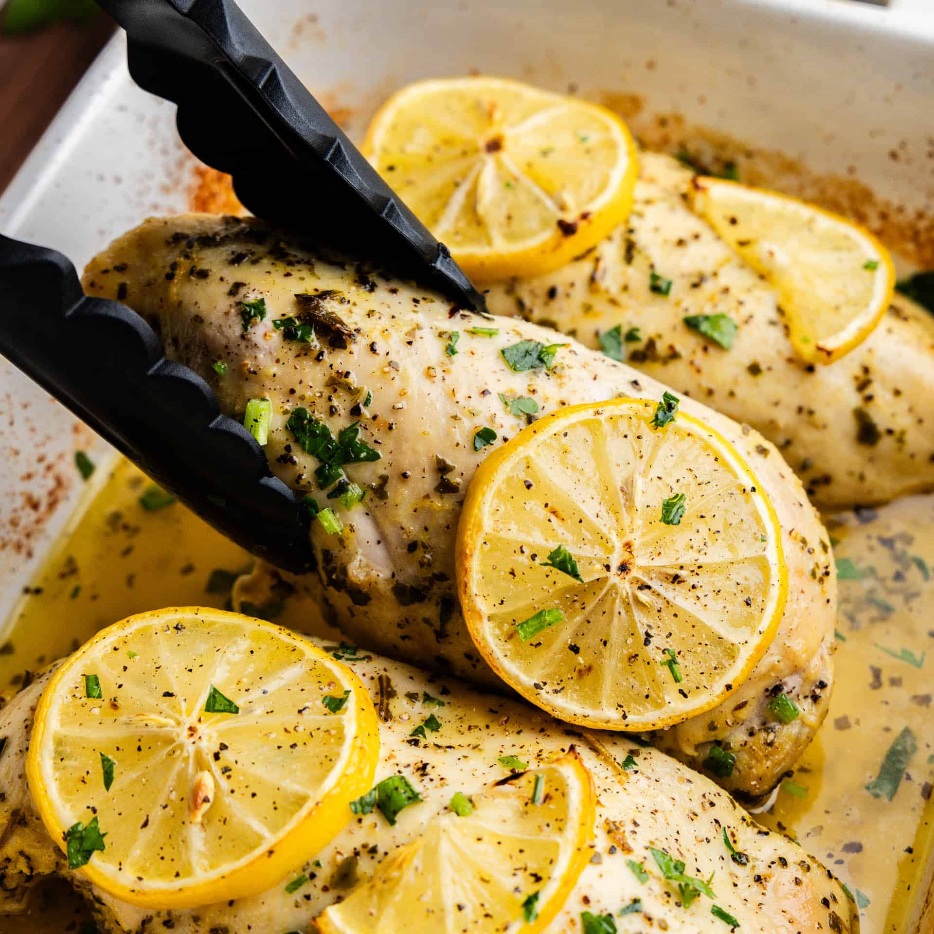 Tongs holding Lemon Herb Baked Chicken Breast.