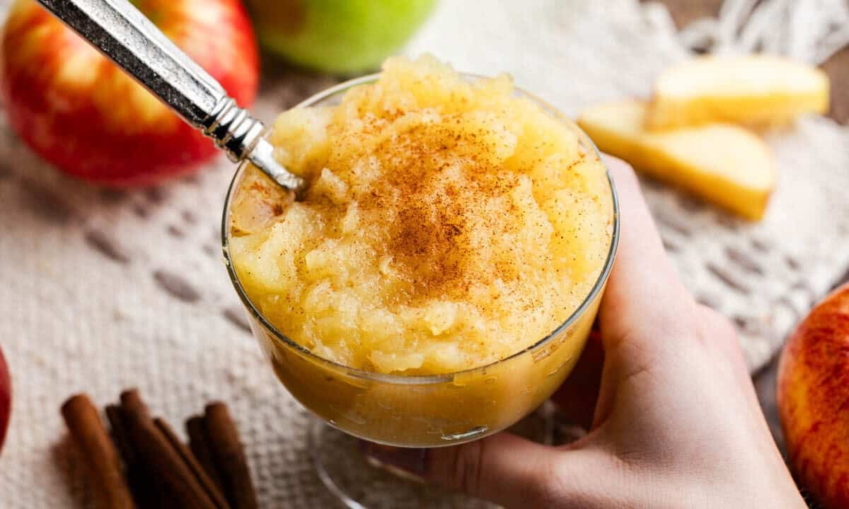 Fancy glass full of applesauce with a spoon in it being held.