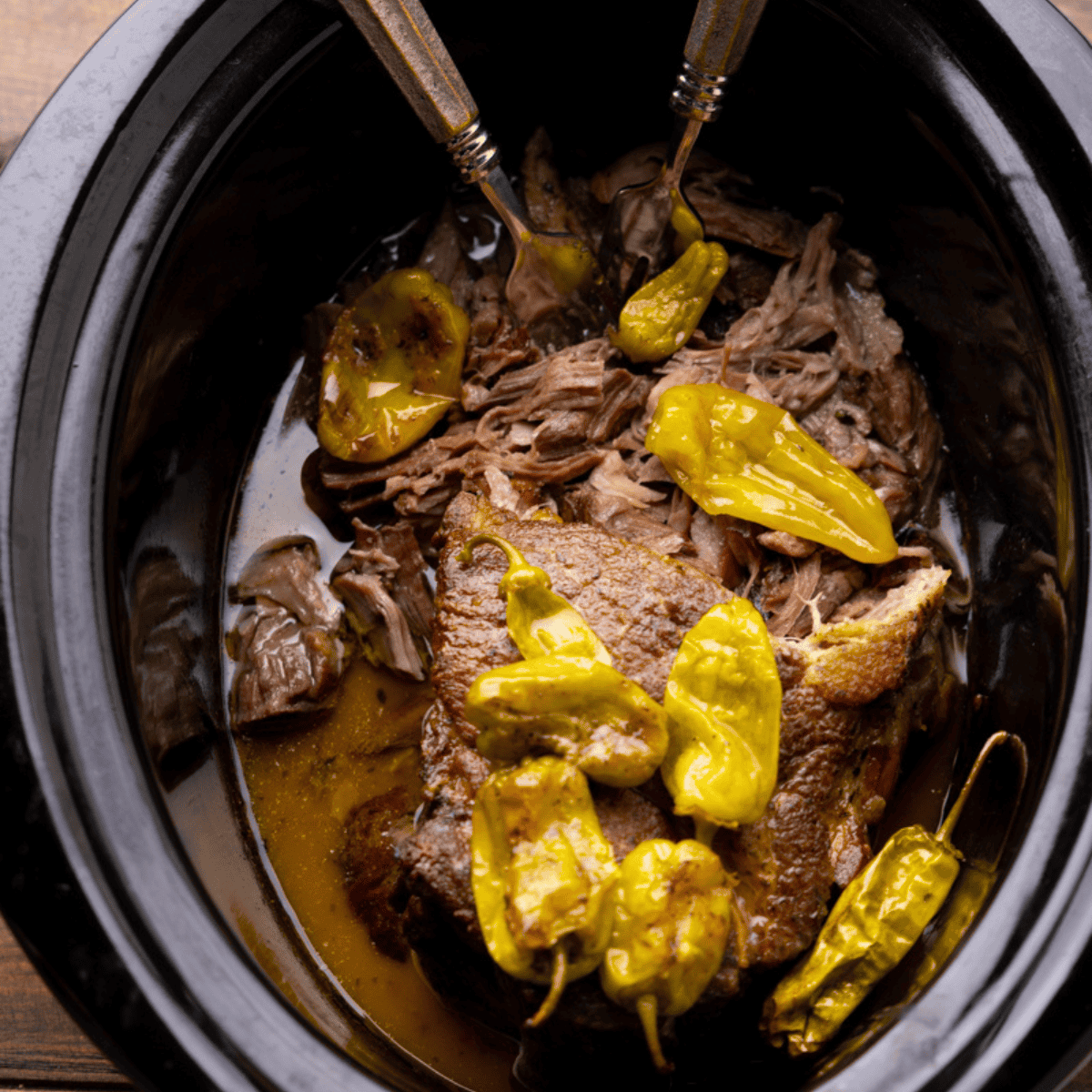 A slow cooker of Mississippi Pork Roast that has been partially shredded by porks.