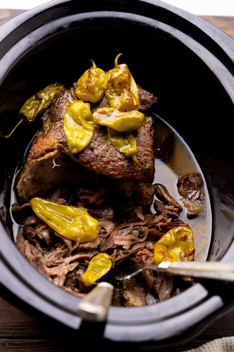 A close up view of a slow cooker of Mississippi Pork Roast that has been partially shredded by porks.