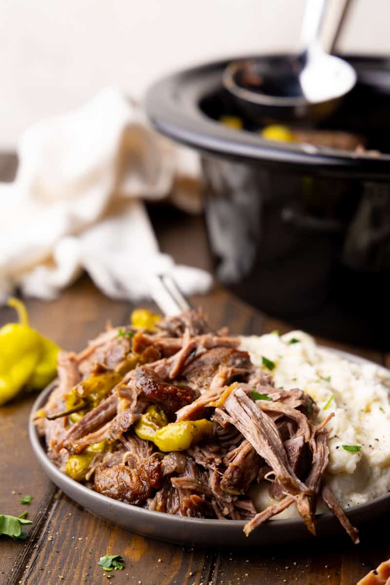 A plate of shredded slow cooker Mississippi pork roast on a plate with mashed potatoes.