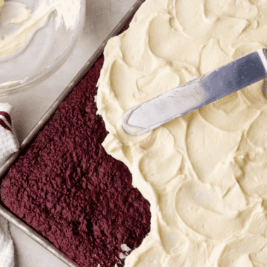 An overhead view of a red velvet sheet cake that is being frosted.