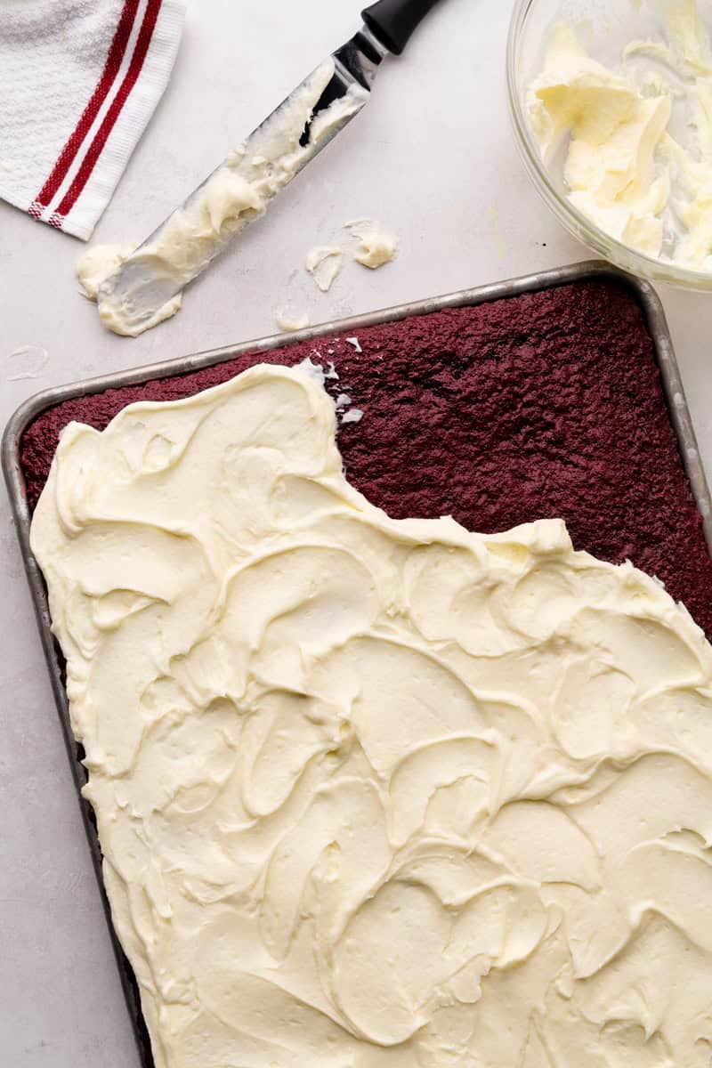 An overhead view of a red velvet sheet cake that has been partially frosted.