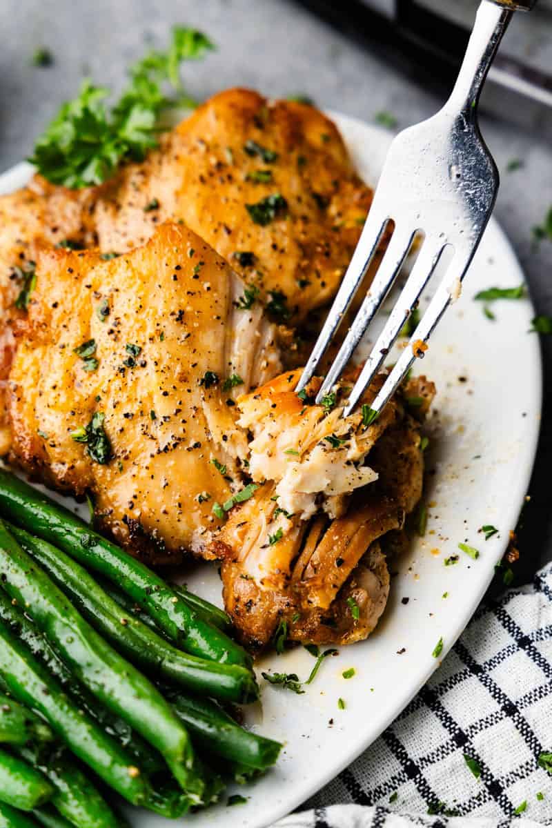 Sheet Pan Boneless Skinless Chicken Thighs piled on a plate with green beans and a fork bite.