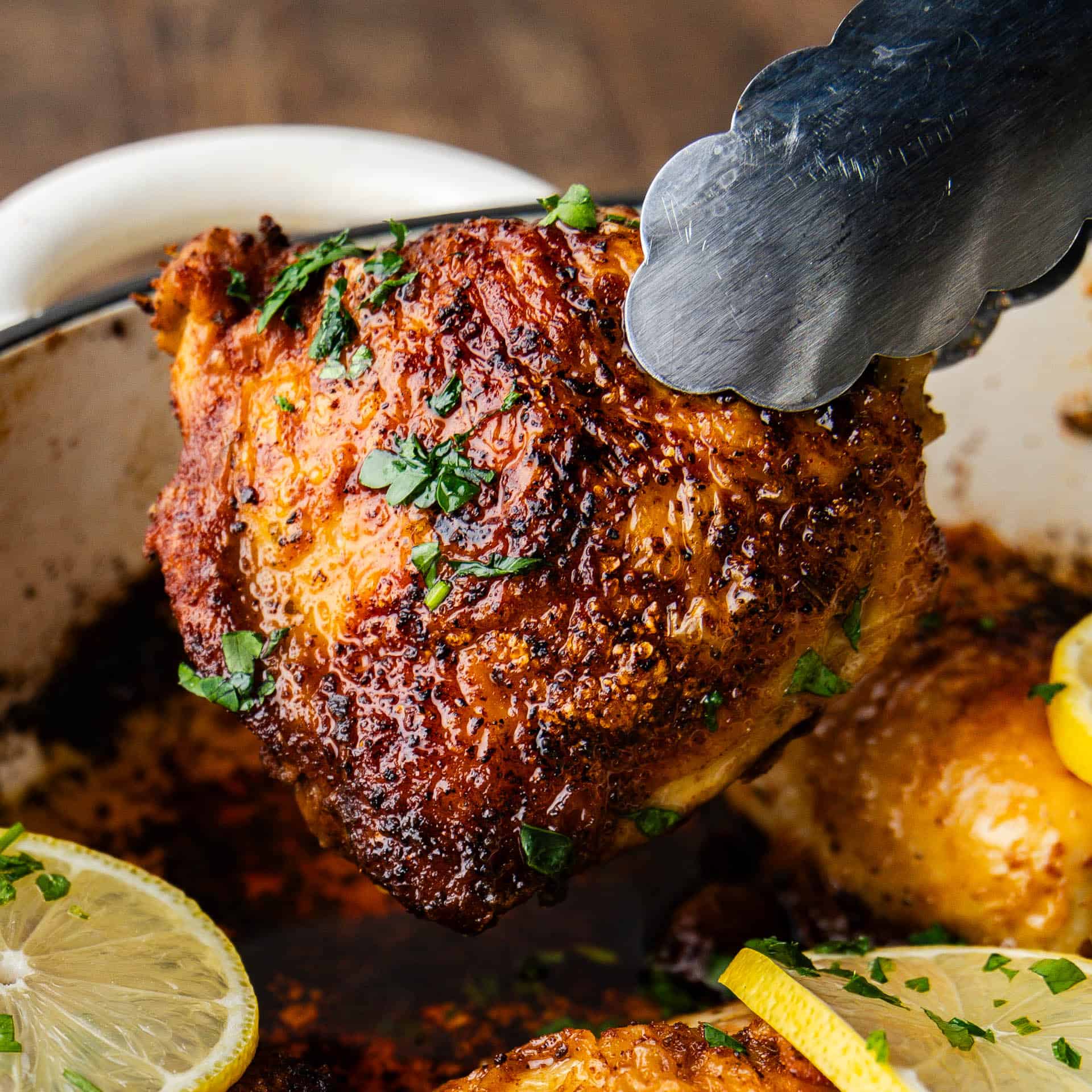 Closeup of Skillet Chicken Thighs being lifted by tongs.