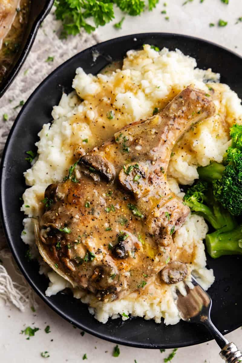 Smothered Pork Chops on a bed of mashed potatoes on a black plate.