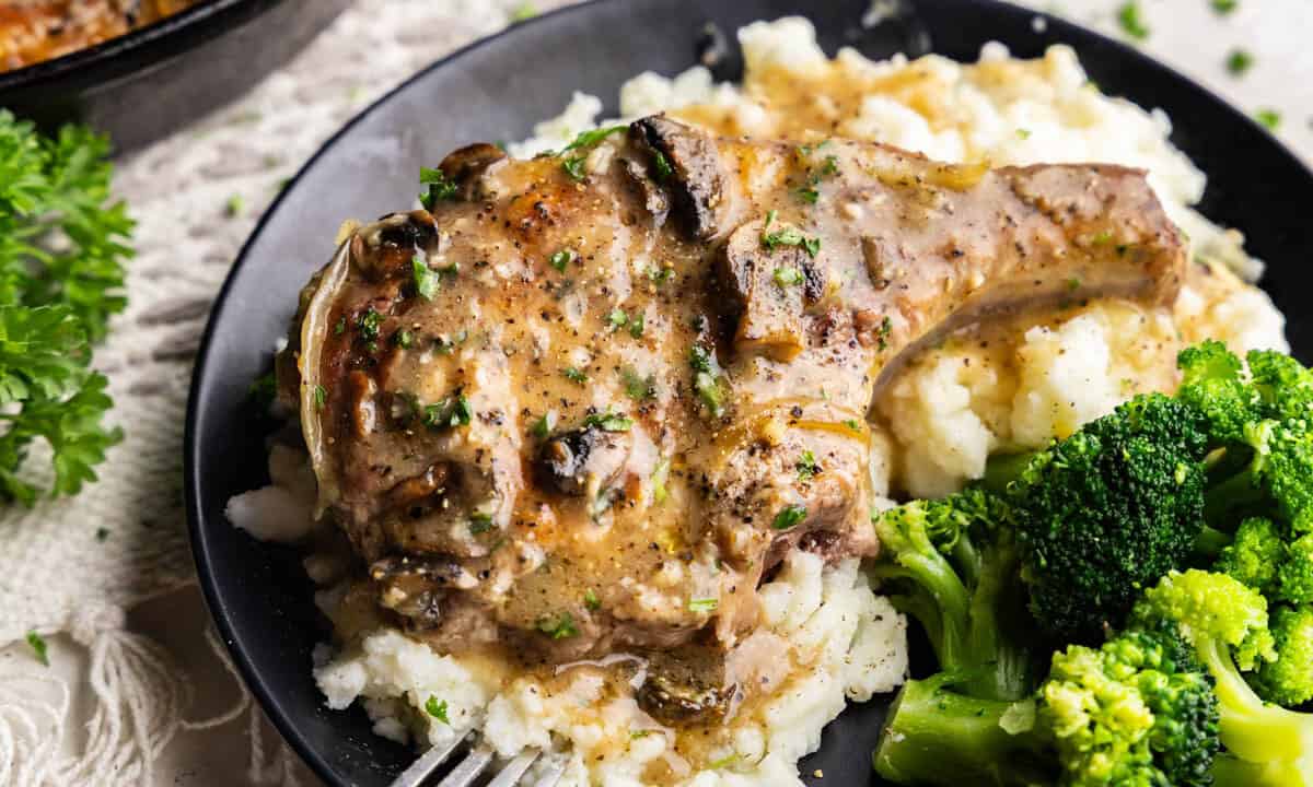 Smothered Pork Chops on a bed of mashed potatoes on a black plate.