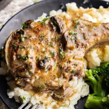 Smothered Pork Chops on a bed of mashed potatoes on a black plate.