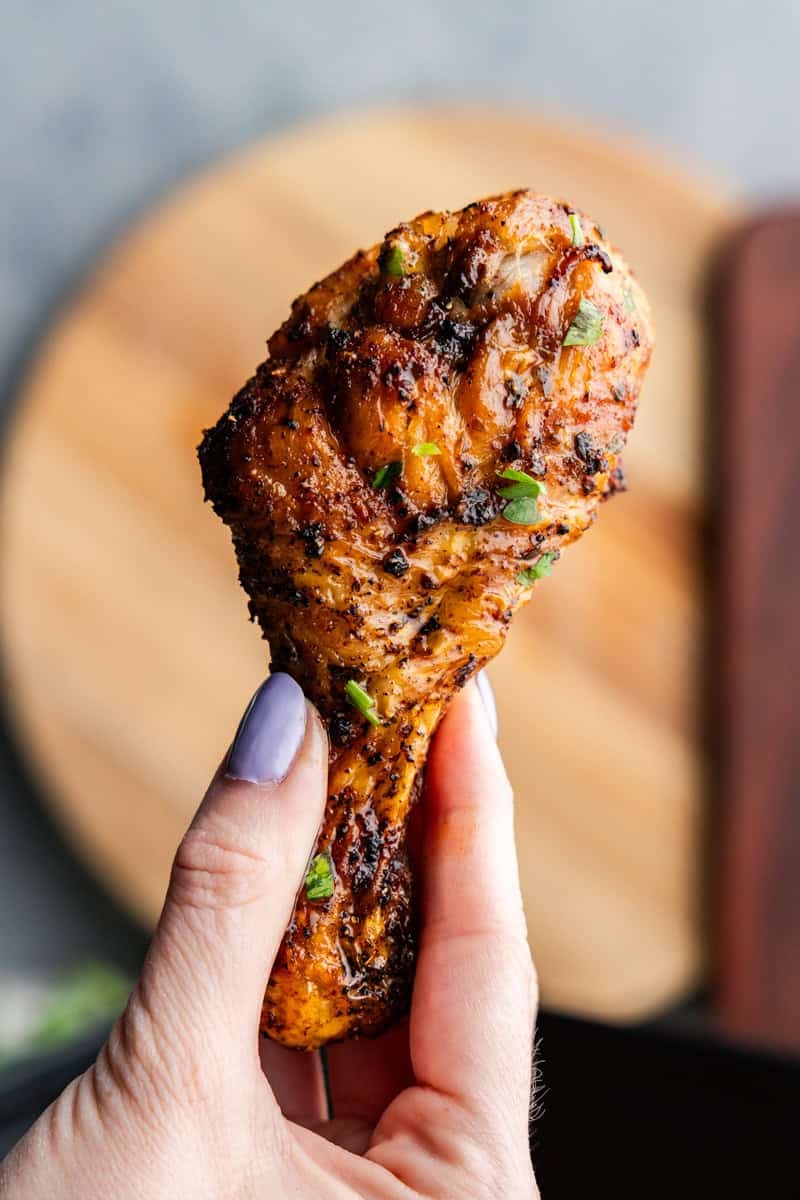 Closeup of a Chicken drumstick being held over the Air Fryer.