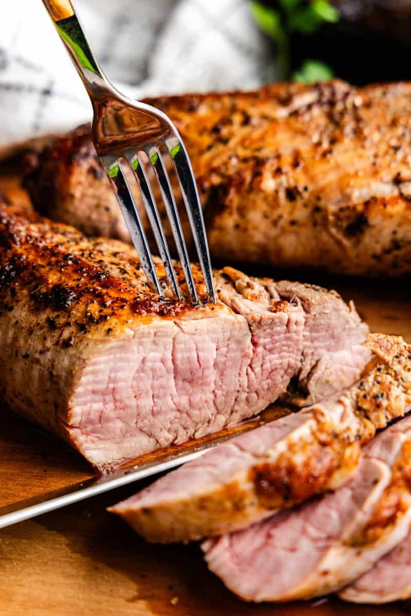 Closeup of Garlic Butter Pork Tenderloin being cut on a cutting board.