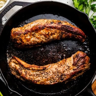 Overhead of Garlic Butter Pork Tenderloin on a skillet with mashed potatoes and asparagus in the background.