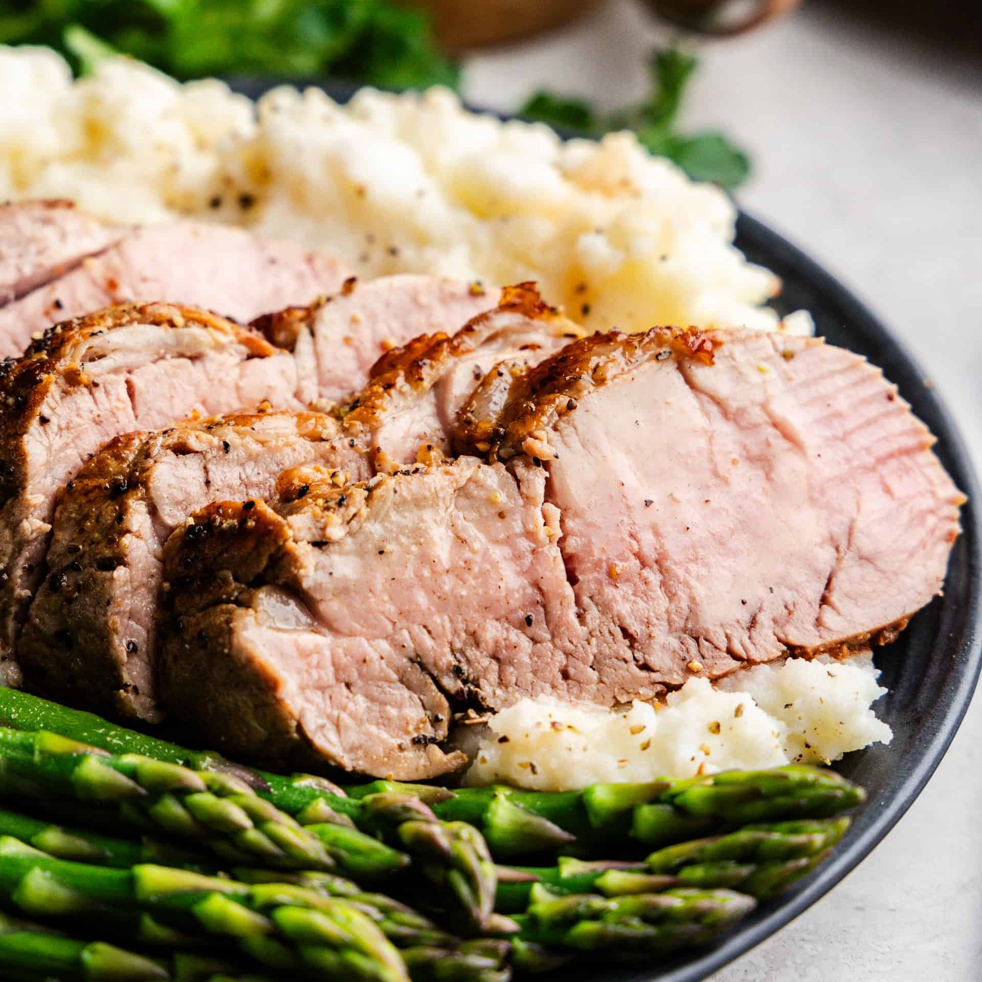 Closeup of Garlic Butter Pork Tenderloin on a plate with mashed potatoes and asparagus.