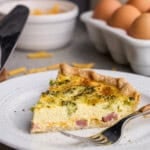 A slice of Ham, Broccoli & Cheddar Quiche on a plate with a fork.