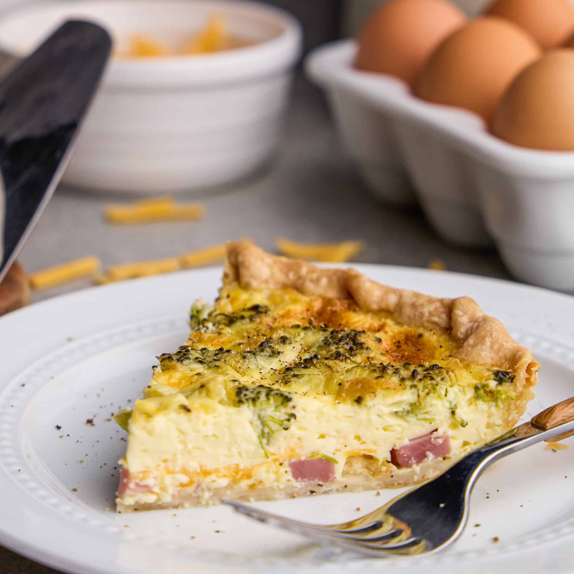 A slice of Ham, Broccoli & Cheddar Quiche on a plate with a fork.