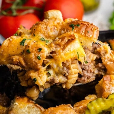 Closeup of ladleful of cheeseburger casserole in cast iron.