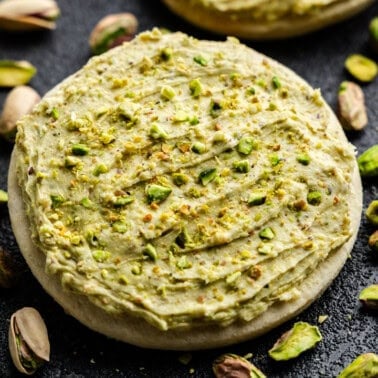 Closeup of Pistachio Buttercream Frosting on a cookie surrounded by pistachios.