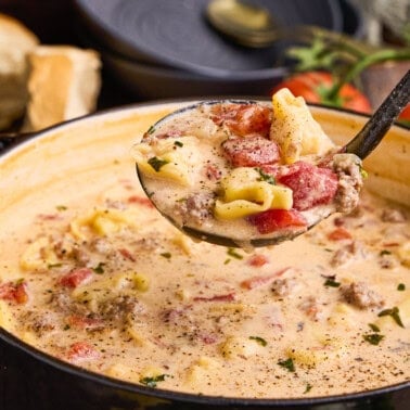 A ladle full of Sausage & Tortellini Soup over a soup pot.