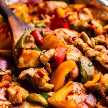 Closeup of Hawaiian Chicken & Veggies on a sheet pan lifted by a wooden spoon.